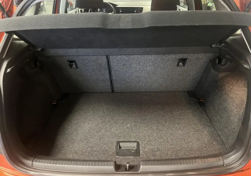 Coffre ouvert d'une Volkswagen Polo orange vue de l'arrière, montrant l'espace de chargement vide et la tablette cache-bagages.