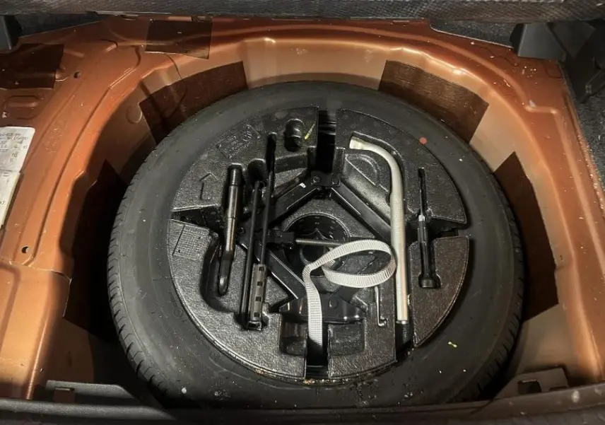 Vue rapprochée de la roue de secours noire et des outils de bord dans le coffre orange de la Volkswagen Polo 2019.