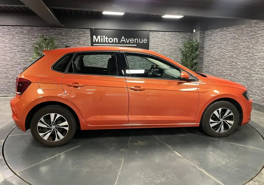 Profil droit d'une Volkswagen Polo orange métallisée 2019 avec jantes alliage et rétroviseurs couleur carrosserie.