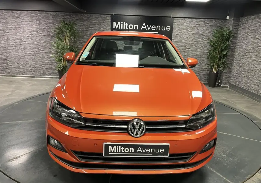 Vue frontale d'une Volkswagen Polo orange métallisée 2019 avec calandre chromée et plaque Milton Avenue.