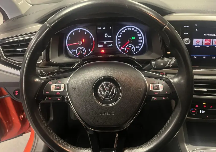 Vue intérieure centrée sur le volant cuir multifonction de la Volkswagen Polo orange avec tableau de bord numérique.