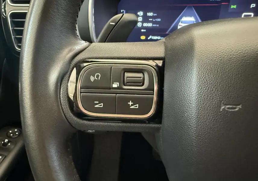 Gros plan sur les commandes gauche du volant cuir noir du Citroën C5 Aircross 2020, tableau de bord numérique en arrière-plan.