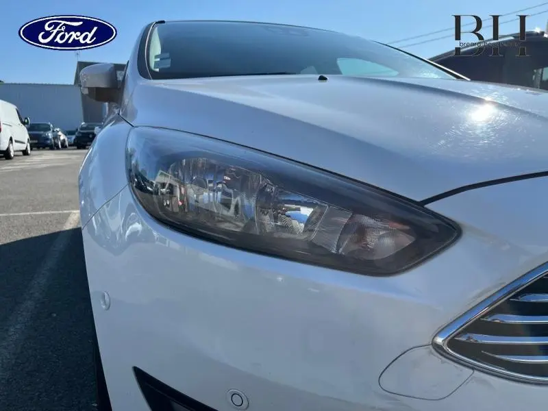 Gros plan sur le phare avant gauche d'une Ford Focus blanc glacier, avec calandre chromée visible.