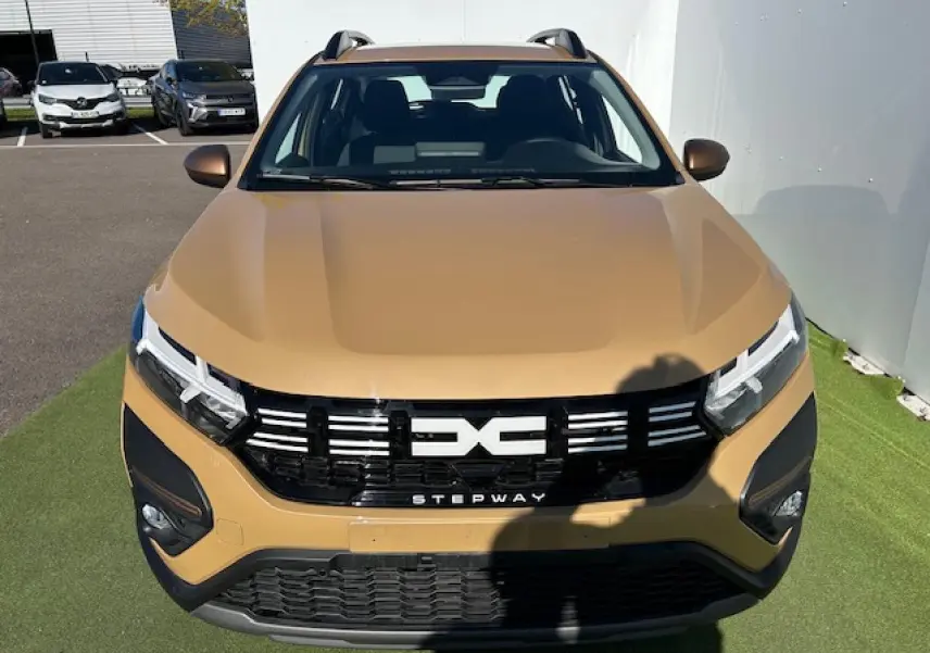 Vue avant rapprochée d'une Dacia Sandero Stepway beige Safari avec calandre noire et logo central distinctif.
