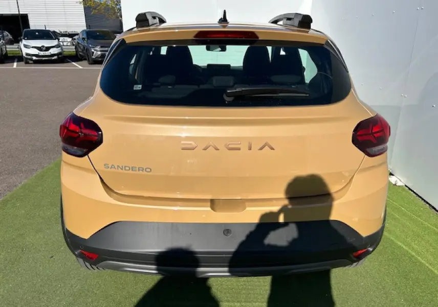 Vue arrière d'une Dacia Sandero beige Safari avec logo et feux arrière LED visibles sur fond extérieur.
