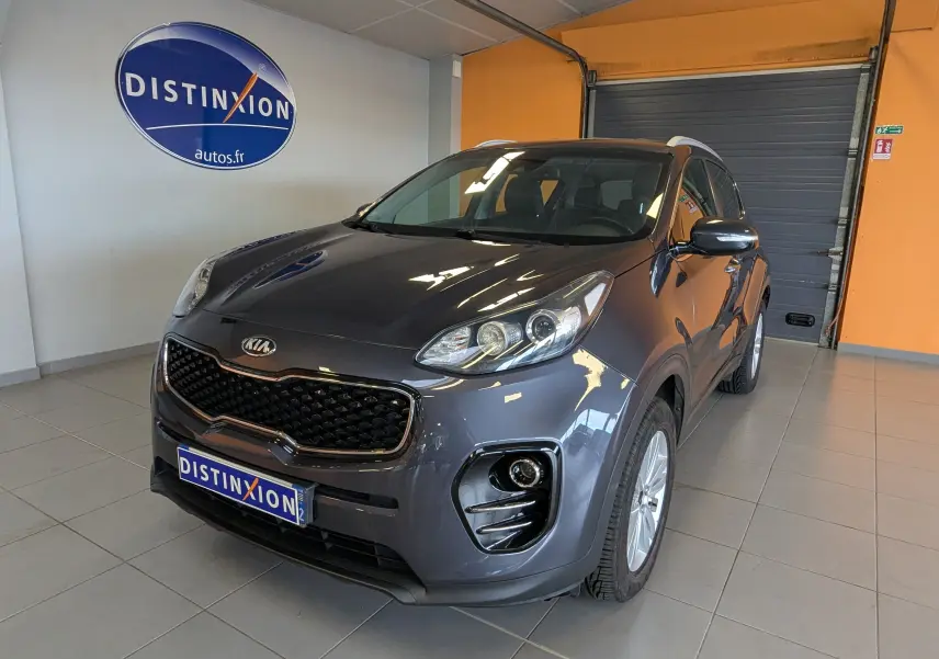KIA Sportage gris en 3/4 avant droit dans un showroom avec calandre noire et jantes argentées.