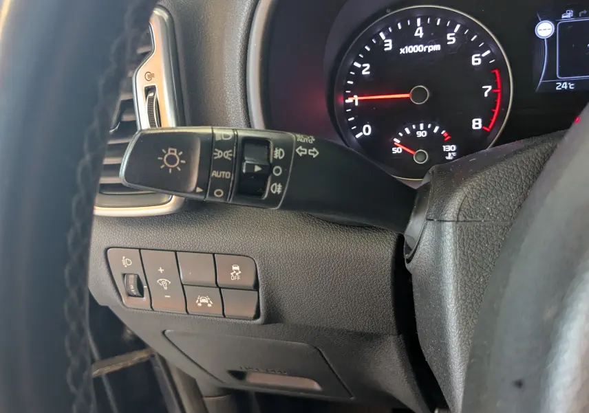 Vue rapprochée du commodo d'éclairage et des boutons de contrôle à gauche du volant dans un Kia Sportage gris de 2016.