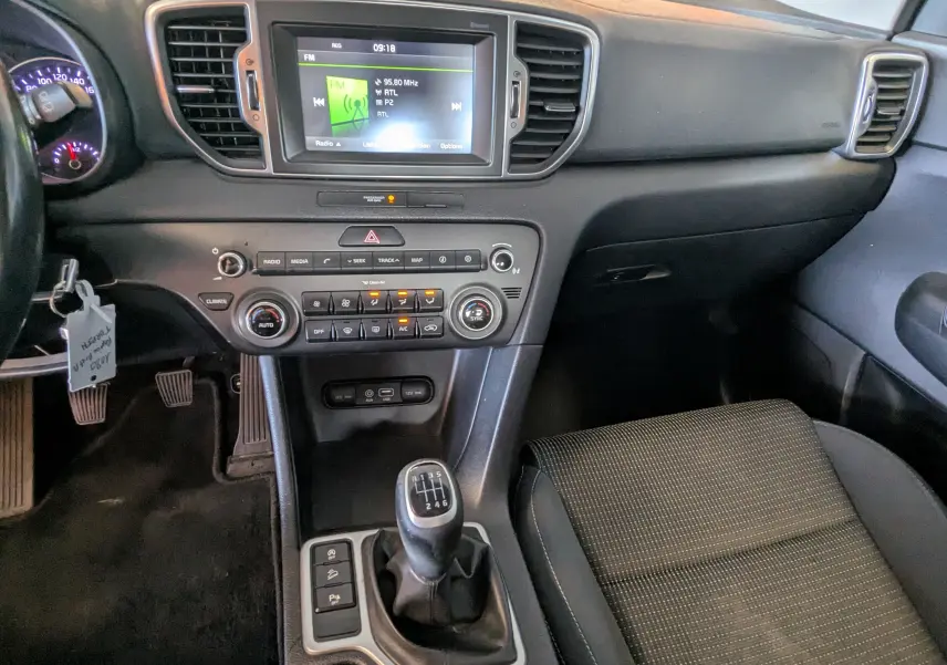 Vue intérieure du tableau de bord et console centrale du Kia Sportage gris 2016, avec écran tactile et boîte manuelle.