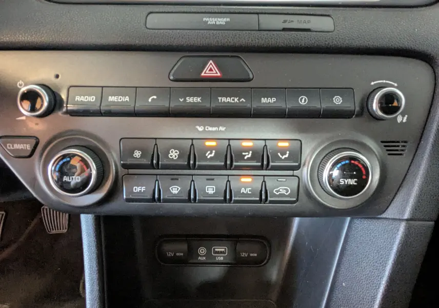 Vue rapprochée de la console centrale du Kia Sportage gris 2016, montrant les commandes climatisation et multimédia avec boutons rétroéclairés.