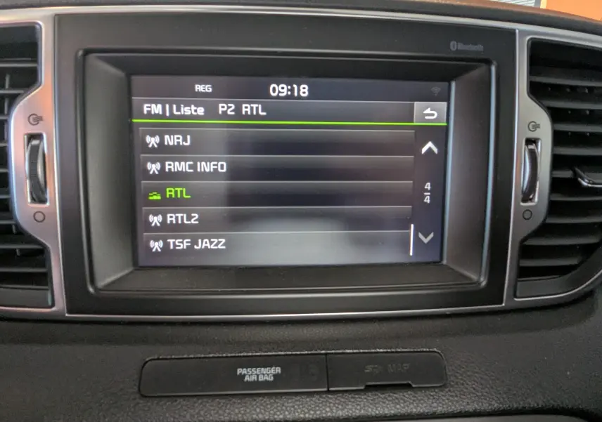 Écran central tactile du tableau de bord du Kia Sportage gris 2016 affichant la liste des stations radio FM.