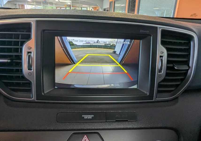 Écran central montrant la caméra de recul du Kia Sportage gris, avec lignes de guidage colorées jaunes et rouges.
