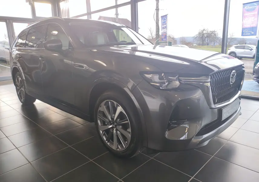 Vue 3/4 avant droit d'un Mazda CX-80 gris foncé hybride rechargeable exposé en showroom avec calandre imposante.