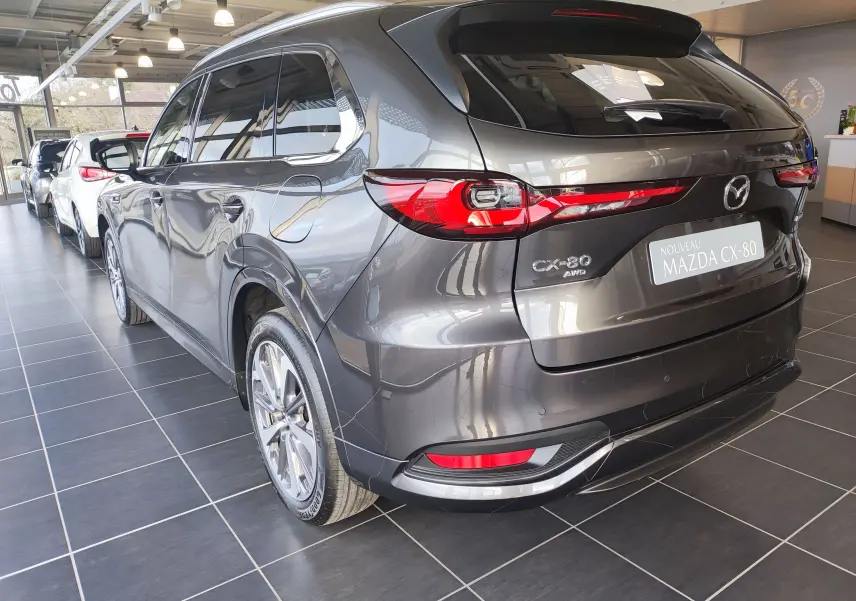 Vue 3/4 arrière droite du Mazda CX-80 gris foncé hybride rechargeable, avec feux arrière allongés et jantes alliage showroom.