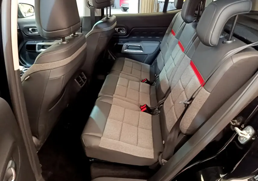 Vue latérale droite de l'intérieur arrière du Citroën C5 Aircross noir, sièges tissu gris avec bandes rouges et appuie-têtes.