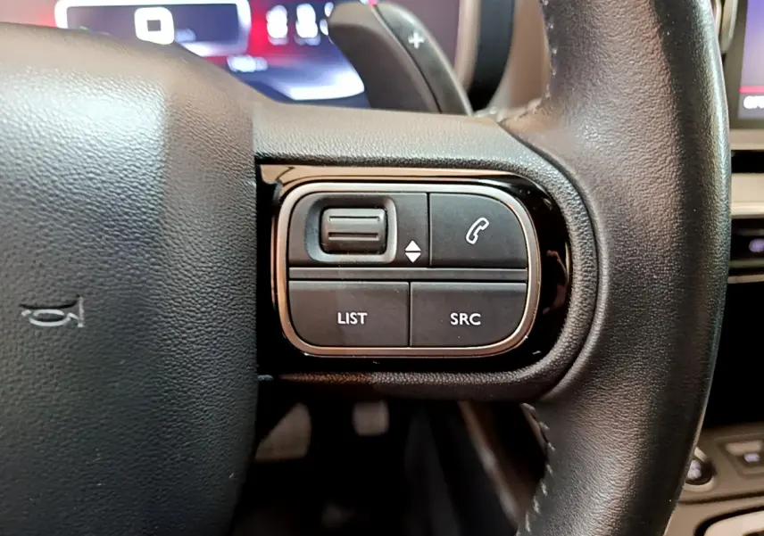 Gros plan sur les commandes gauche du volant cuir noir du Citroën C5 Aircross 2020 avec affichage digital en arrière-plan.