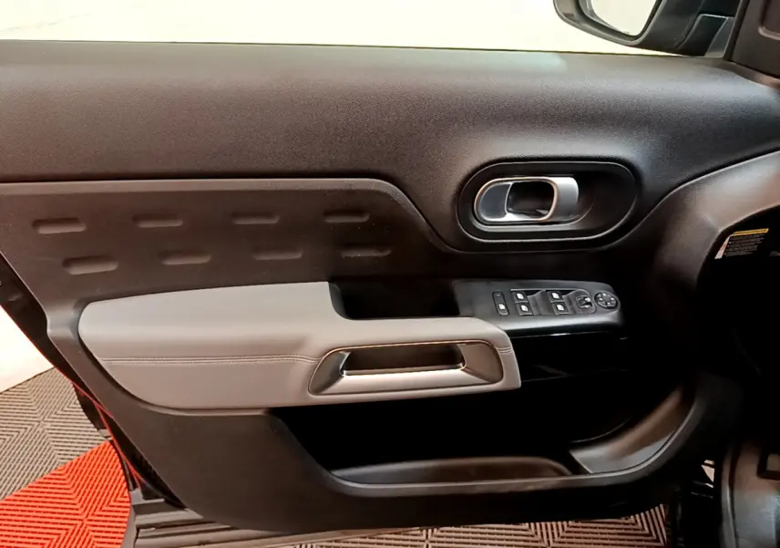 Gros plan sur la porte côté gauche intérieure du Citroën C5 Aircross noir, avec poignée argentée et commandes de vitres.