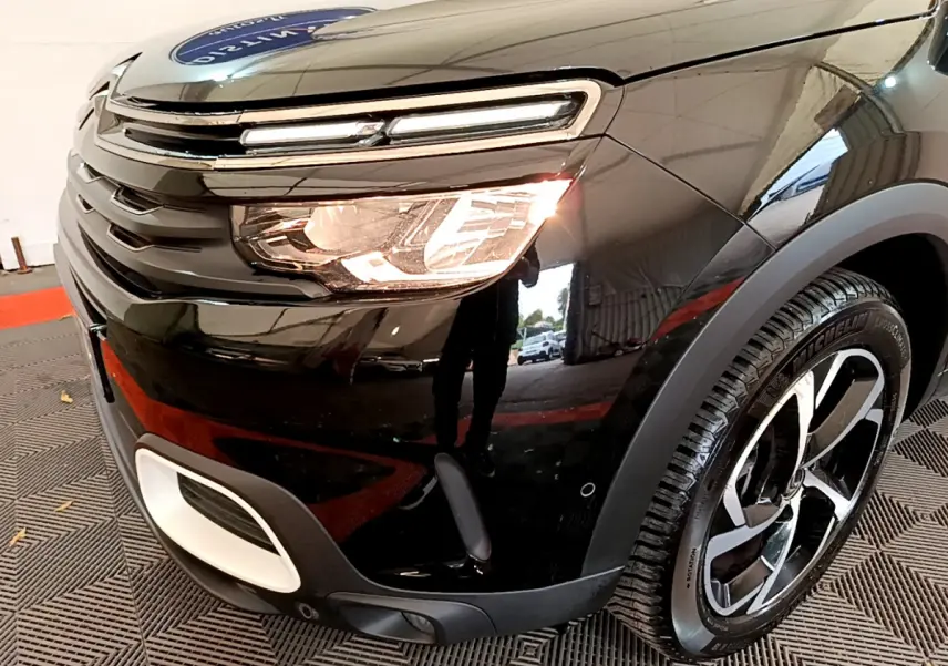 Vue 3/4 avant droit du Citroën C5 Aircross noir, mettant en valeur son phare allumé et sa jante moderne.