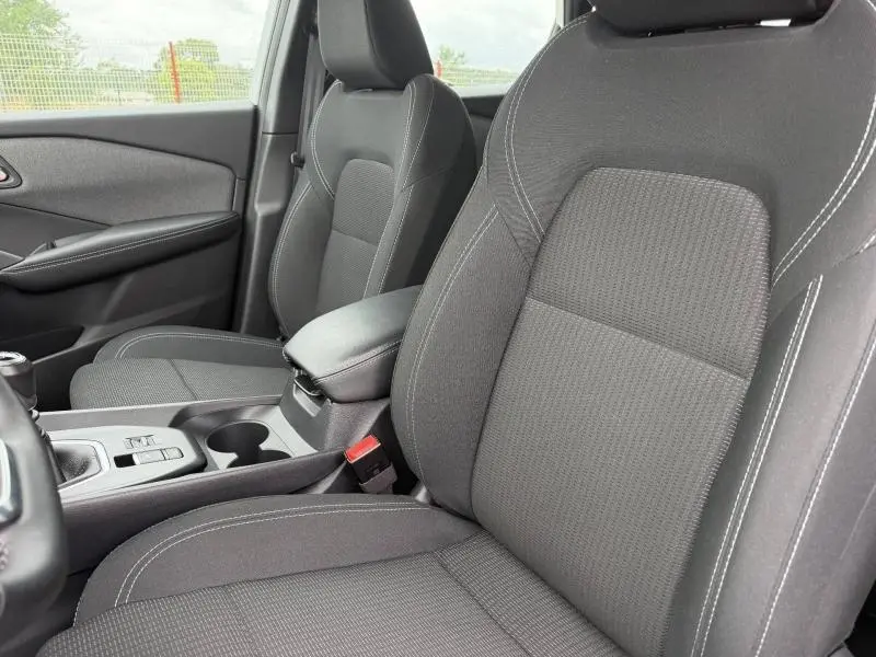 Vue intérieure rapprochée des sièges avant noirs en tissu du Nissan Qashqai 2025 avec accoudoir central et console.