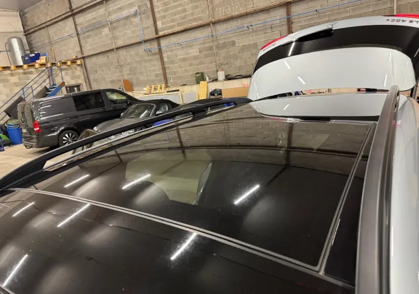 Vue rapprochée du toit panoramique noir du Mercedes GLE 400 E Hybrid argent, avec hayon arrière ouvert en intérieur.