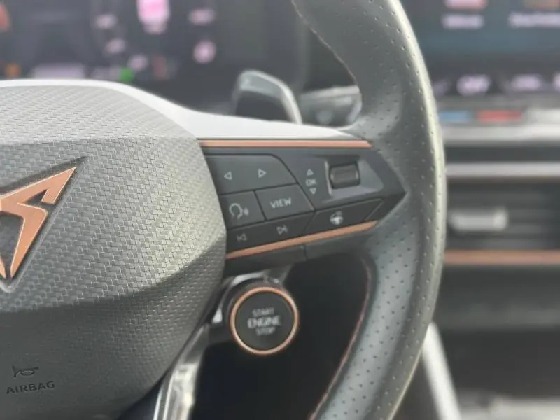 Gros plan sur le volant cuir perforé noir avec commandes multifonctions et bouton start/stop cuivré du CUPRA Formentor.
