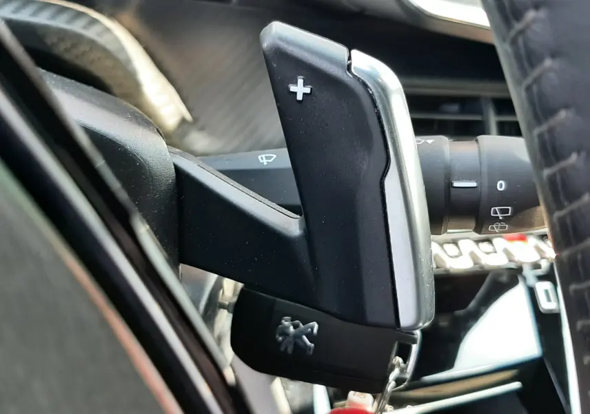 Gros plan sur la palette de changement de vitesse droite avec symbole plus dans l'habitacle noir du Peugeot 2008 gris platinium.