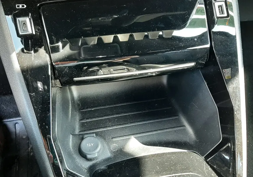 Gros plan sur la console centrale noire brillante avec prise 12V et ports USB du Peugeot 2008 gris platinium 2023