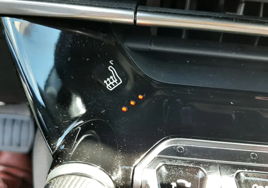 Gros plan sur la commande de siège chauffant avec trois voyants rouges allumés dans l'habitacle noir du Peugeot 2008 gris platinium.