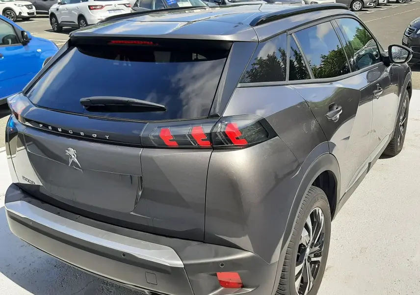 Vue 3/4 arrière droite d'un Peugeot 2008 gris platinium avec feux arrière LED et vitres teintées sur parking.