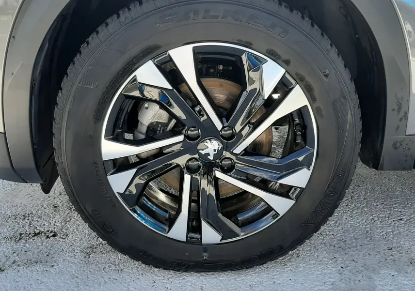 Gros plan sur la roue avant gauche du Peugeot 2008 gris platinium, mettant en valeur la jante alliage noire et argentée au design moderne.