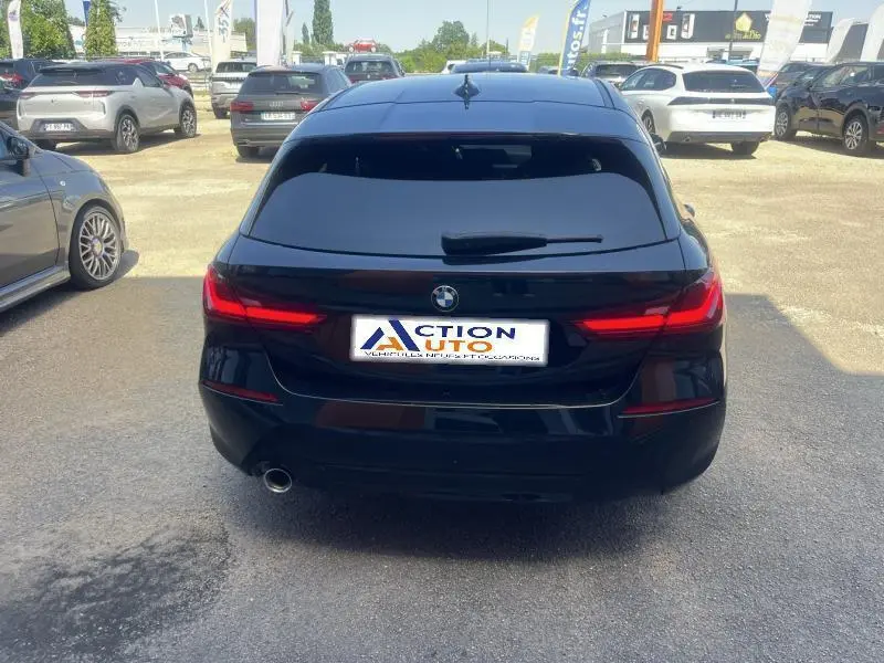 Vue arrière d'une BMW Série 1 noire avec feux arrière LED allumés sur un parking extérieur.