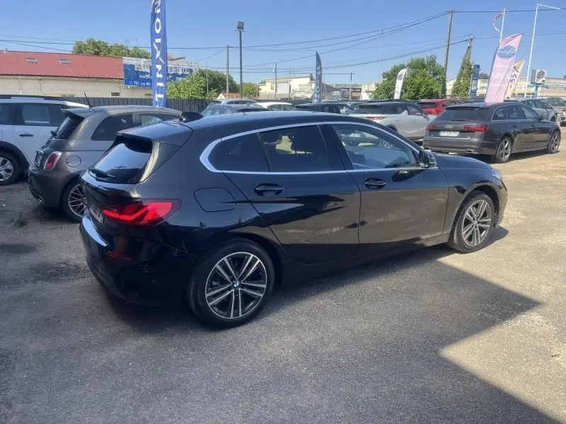 BMW Série 1 noire vue de profil côté droit sur un parking, avec jantes alliage et vitres teintées.