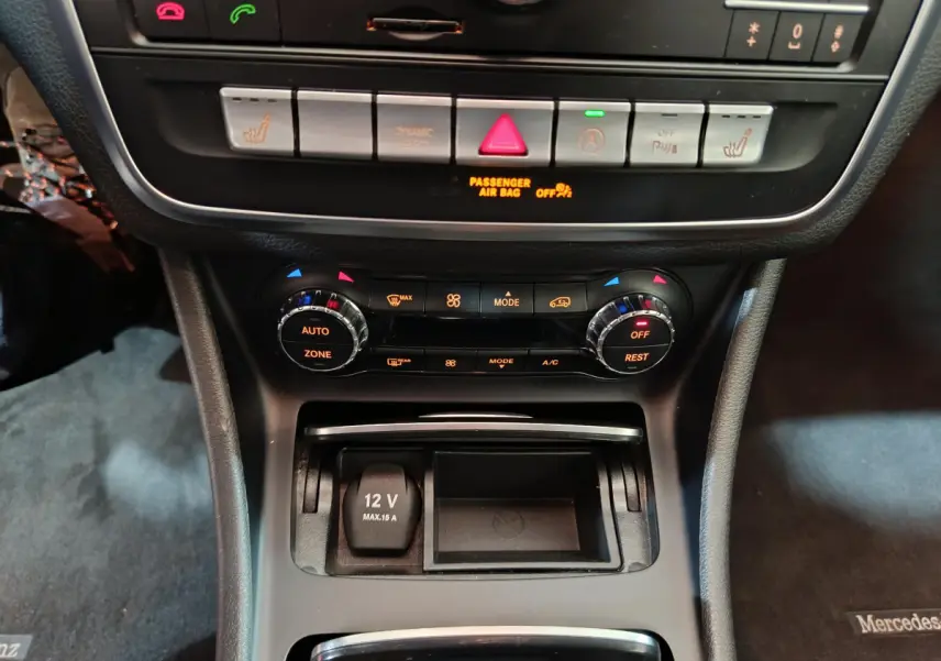 Vue rapprochée de la console centrale noire du Mercedes GLA 200 d, avec commandes climatisation et prise 12V visible.