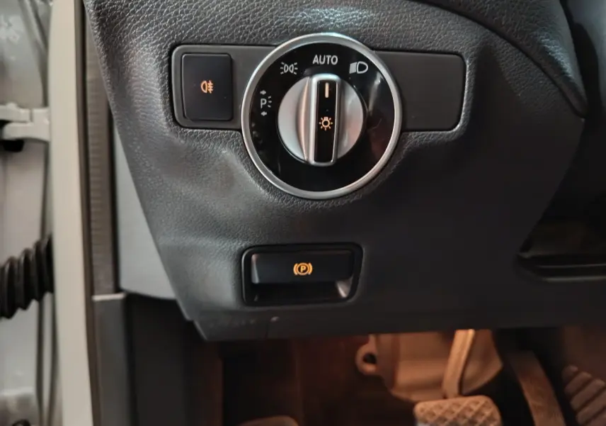Gros plan sur le tableau de bord côté gauche du Mercedes GLA 200 d gris clair, avec commandes des phares et frein électrique.