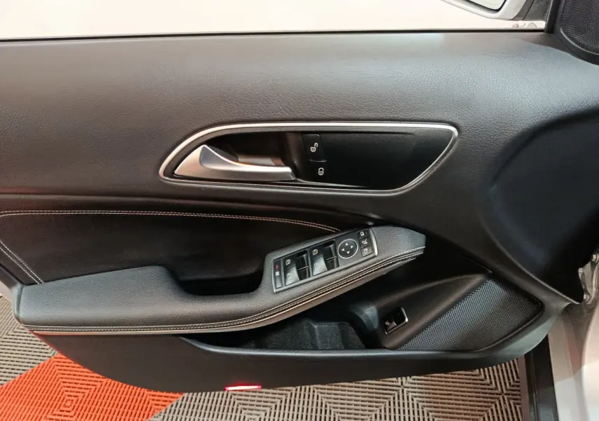 Gros plan sur la porte côté conducteur du Mercedes GLA 200 d gris clair, montrant les commandes de vitres et la poignée intérieure chrome.