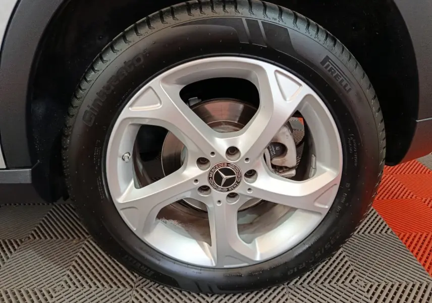 Gros plan sur la roue arrière droite d'un Mercedes GLA 200 d gris clair, avec passage de roue noir et sol en damier rouge et gris.