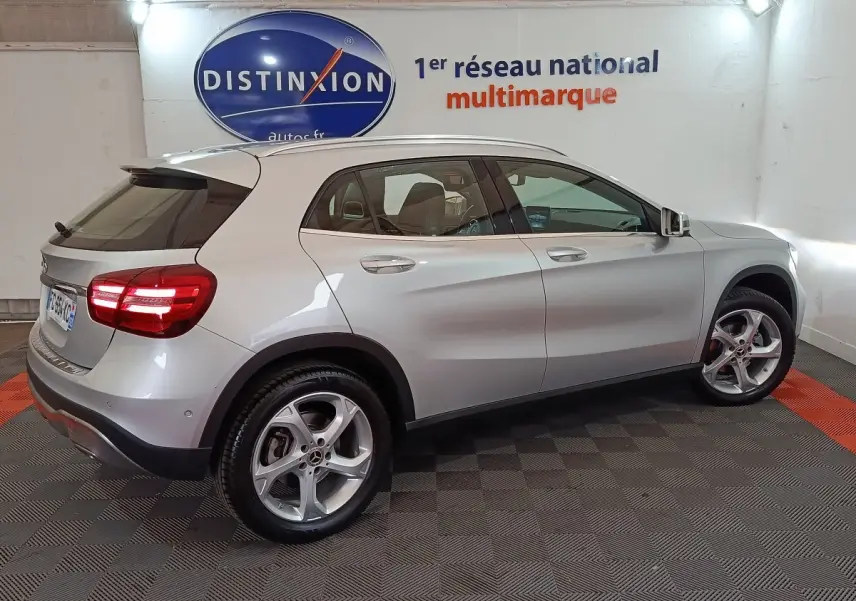 Vue latérale côté droit d'un Mercedes GLA 200 d gris clair 2018 avec jantes alliage et feux arrière allumés en intérieur showroom.