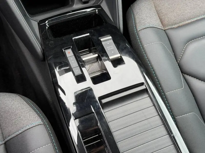 Vue rapprochée de la console centrale noire brillante et des sièges gris avec surpiqûres bleues du Citroën C4 X 2024.