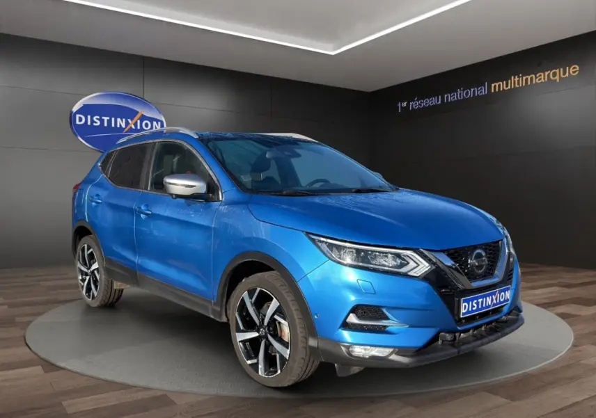 Nissan Qashqai bleu en 3/4 avant droit, avec jantes alliage noires et rétroviseurs argentés, sur podium intérieur.