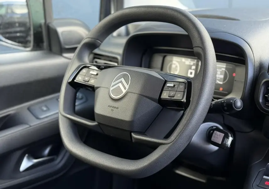 Vue rapprochée du volant multifonctions noir du Citroën Berlingo 2025, côté conducteur avec tableau de bord numérique flou.
