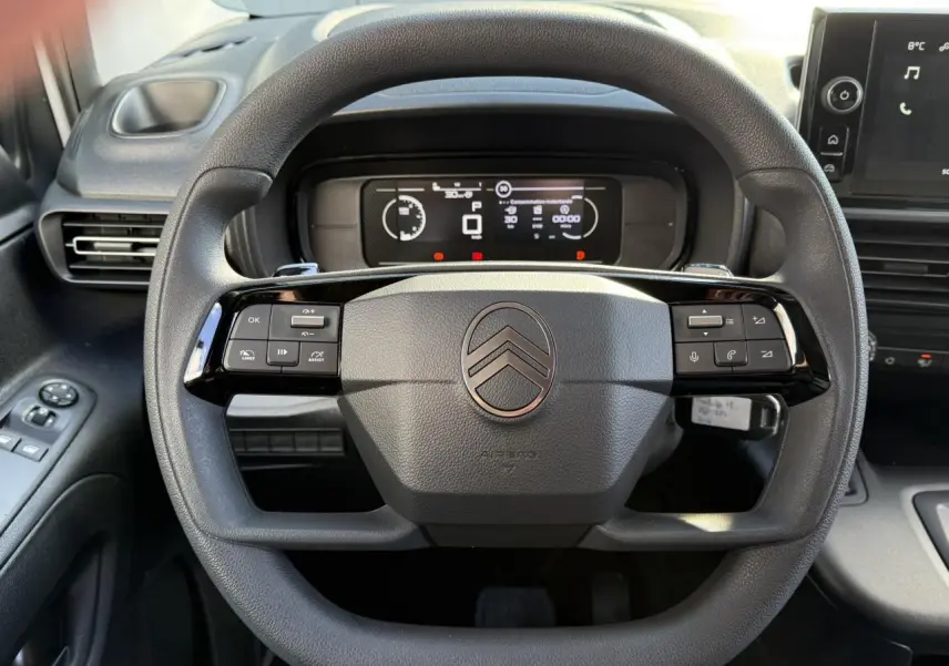 Vue rapprochée du volant multifonctions noir du Citroën Berlingo 2025 avec tableau de bord numérique en arrière-plan.