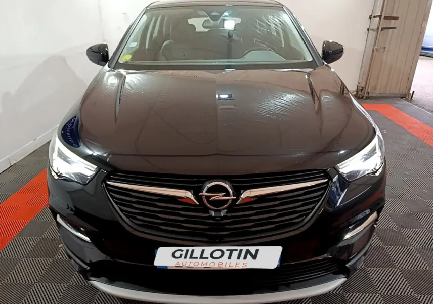 Vue frontale d'un Opel Grandland X noir avec phares LED allumés et calandre chromée dans un garage.