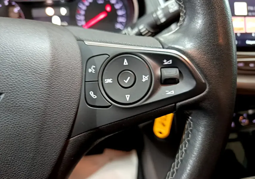 Gros plan sur les commandes gauche du volant cuir noir de l'Opel Grandland X 2021 avec tableau de bord en arrière-plan flou.