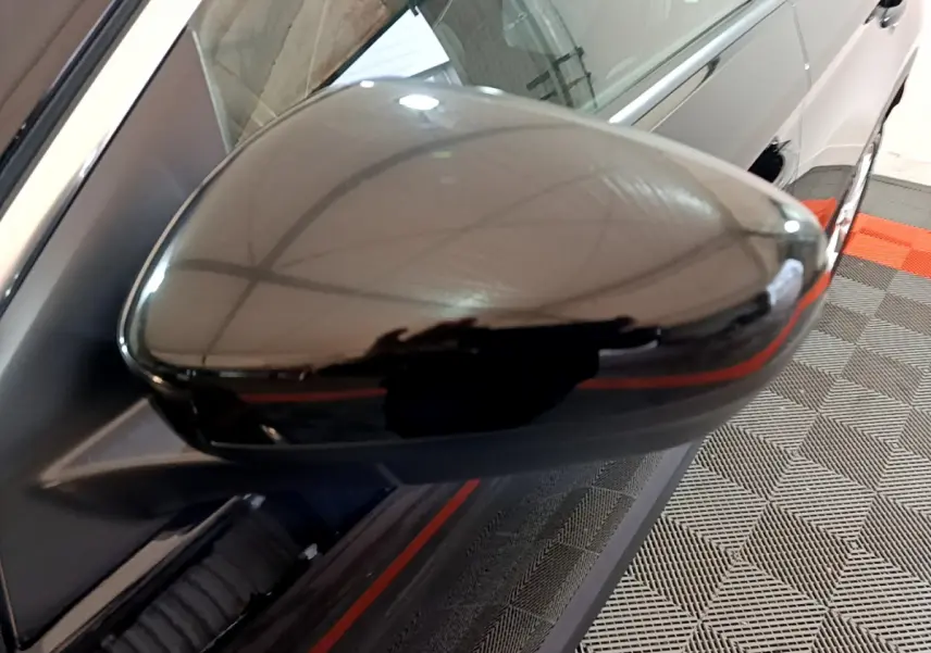 Rétroviseur noir brillant côté gauche en gros plan sur Opel Grandland X noir, reflet de l'environnement intérieur visible.