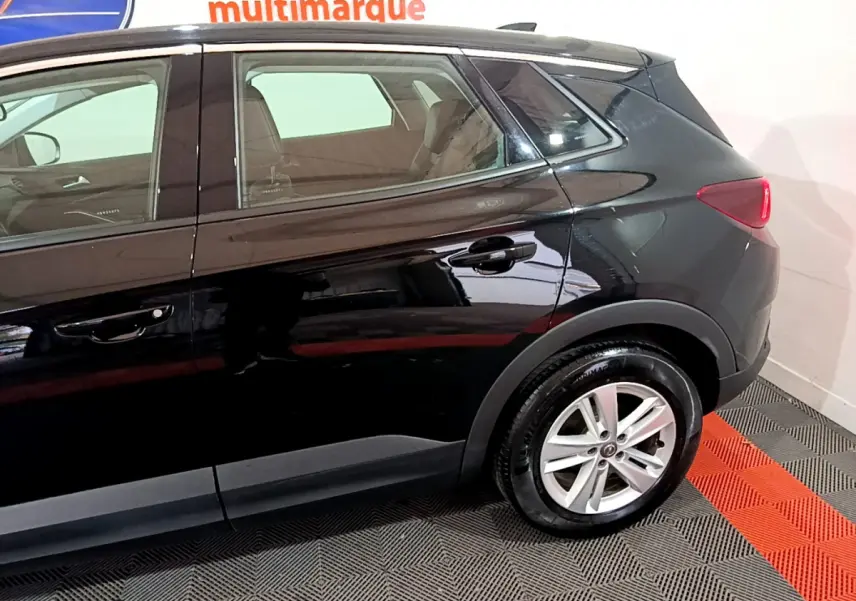 Vue latérale côté droit d'un Opel Grandland X noir avec jantes alliage et feux arrière LED visibles en intérieur showroom.