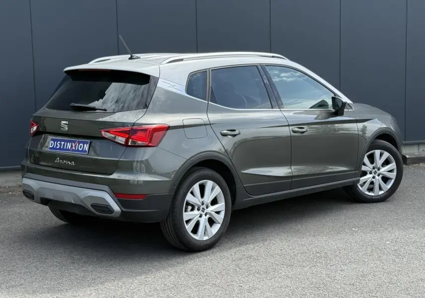 Vue 3/4 arrière droite du SEAT Arona gris Cliff avec toit blanc et jantes alliage 17 pouces sur fond urbain.