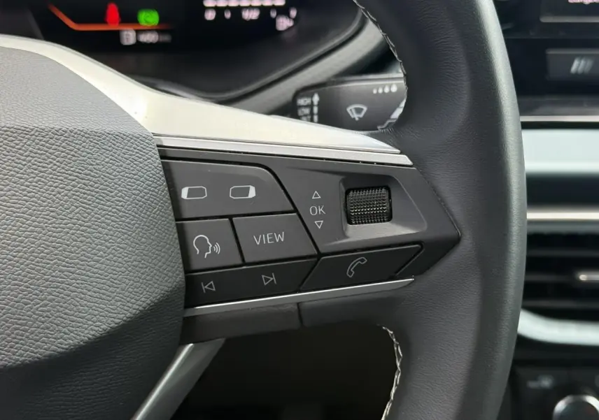Gros plan sur les commandes à droite du volant noir du SEAT Arona 2025, avec affichage digital en arrière-plan.