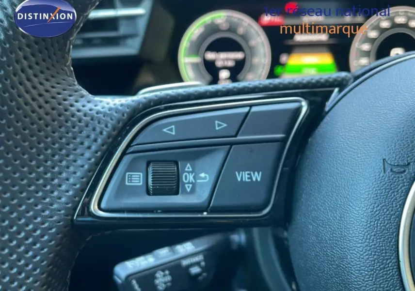 Gros plan sur les commandes du volant en cuir perforé de l'Audi A3 Sportback noir mito metal, tableau de bord numérique en arrière-plan flou.