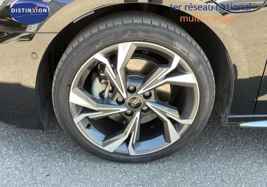 Gros plan sur la roue avant droite d'une Audi A3 Sportback noire, mettant en valeur la jante en alliage au design moderne.