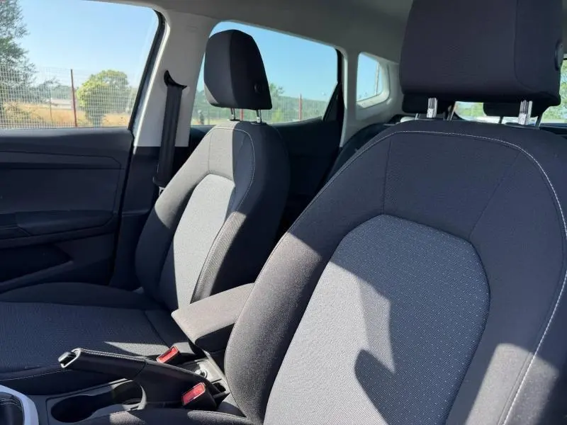 Vue intérieure rapprochée des sièges avant tissu gris du SEAT Arona 2025, avec accoudoir central et ceintures visibles.