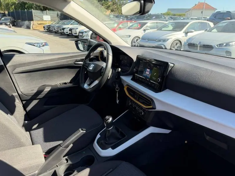 Vue intérieure côté conducteur du SEAT Arona 2025, tableau de bord noir et blanc avec écran tactile et volant cuir multifonction.